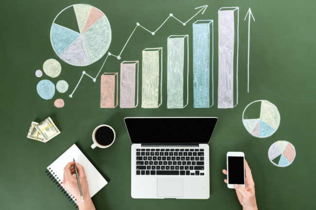 Top view of business person using digital devices at workplace with colorful graphs, home office